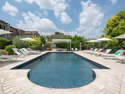 Piscina all’aperto con lettini e ombrelloni nel nostro boutique hotel in Umbria, circondata da un giardino curato e case in pietra.